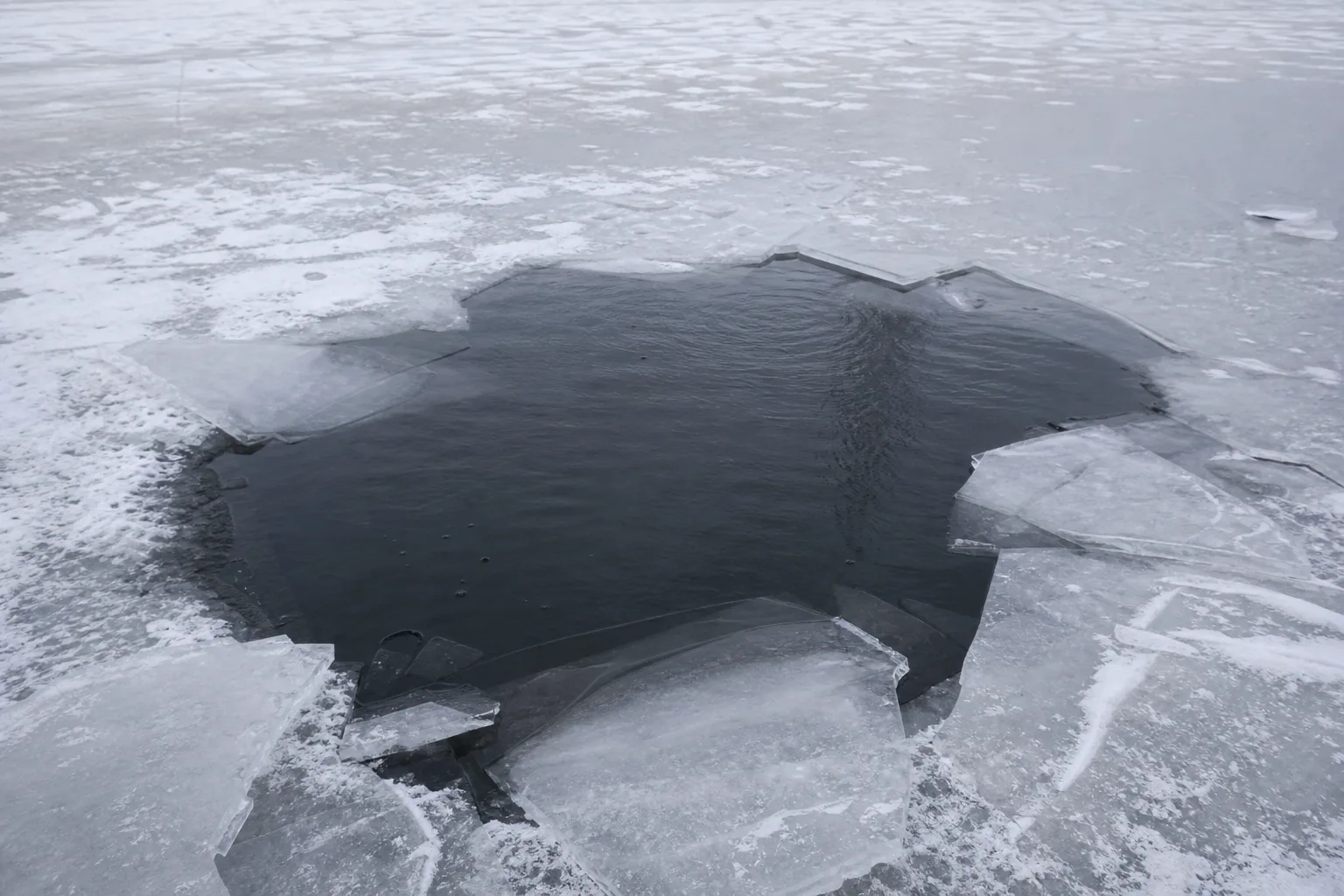 A broken hole in pond ice with dark water beneath