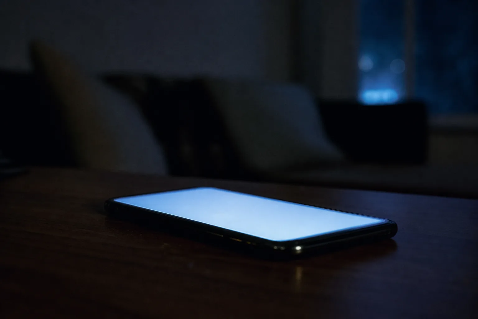 A smartphone glowing faintly on a table in a dim room